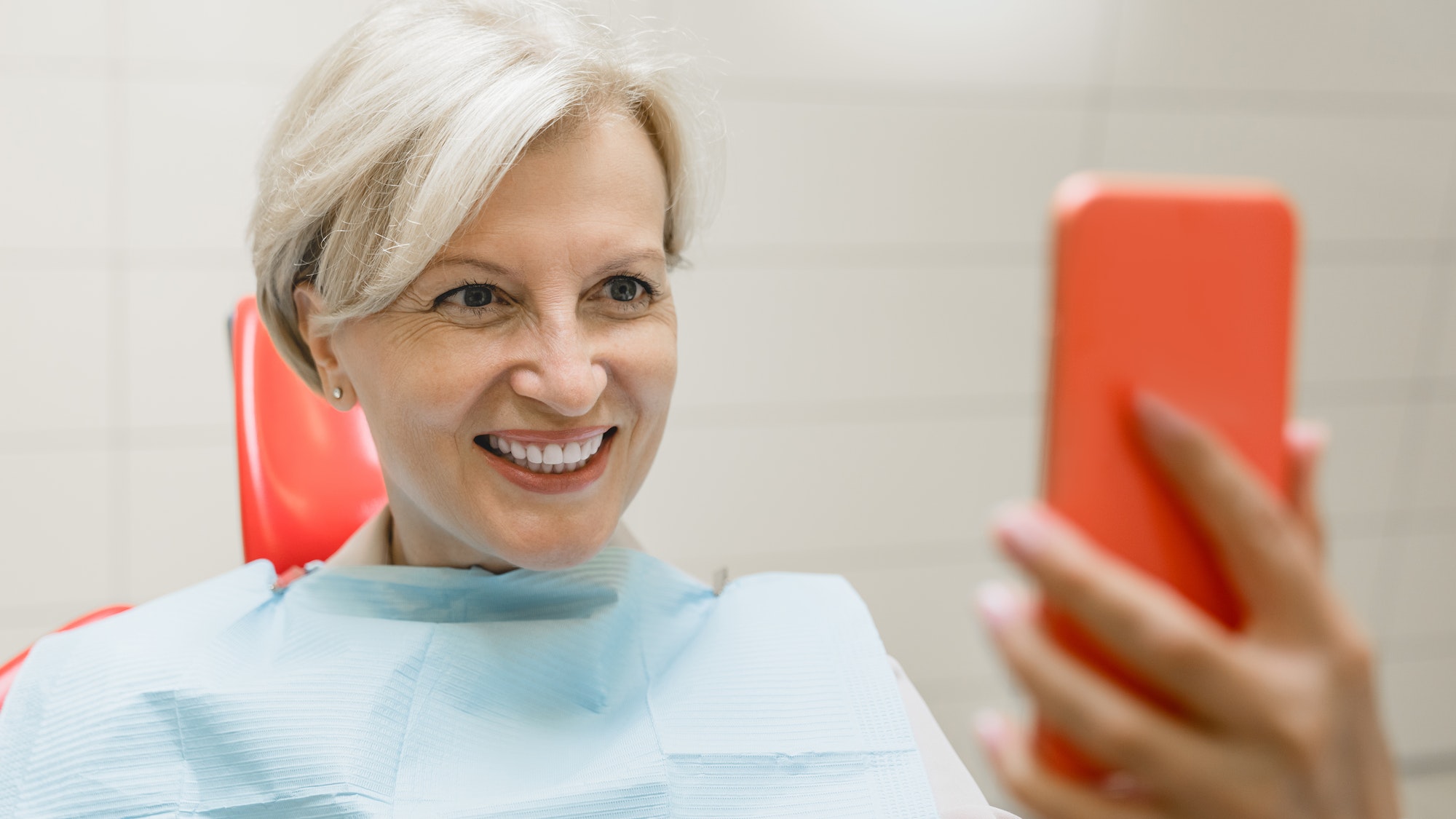 Patient with perfect smile taking selfie vlogging on smart phone at dental stomatological checkup.
